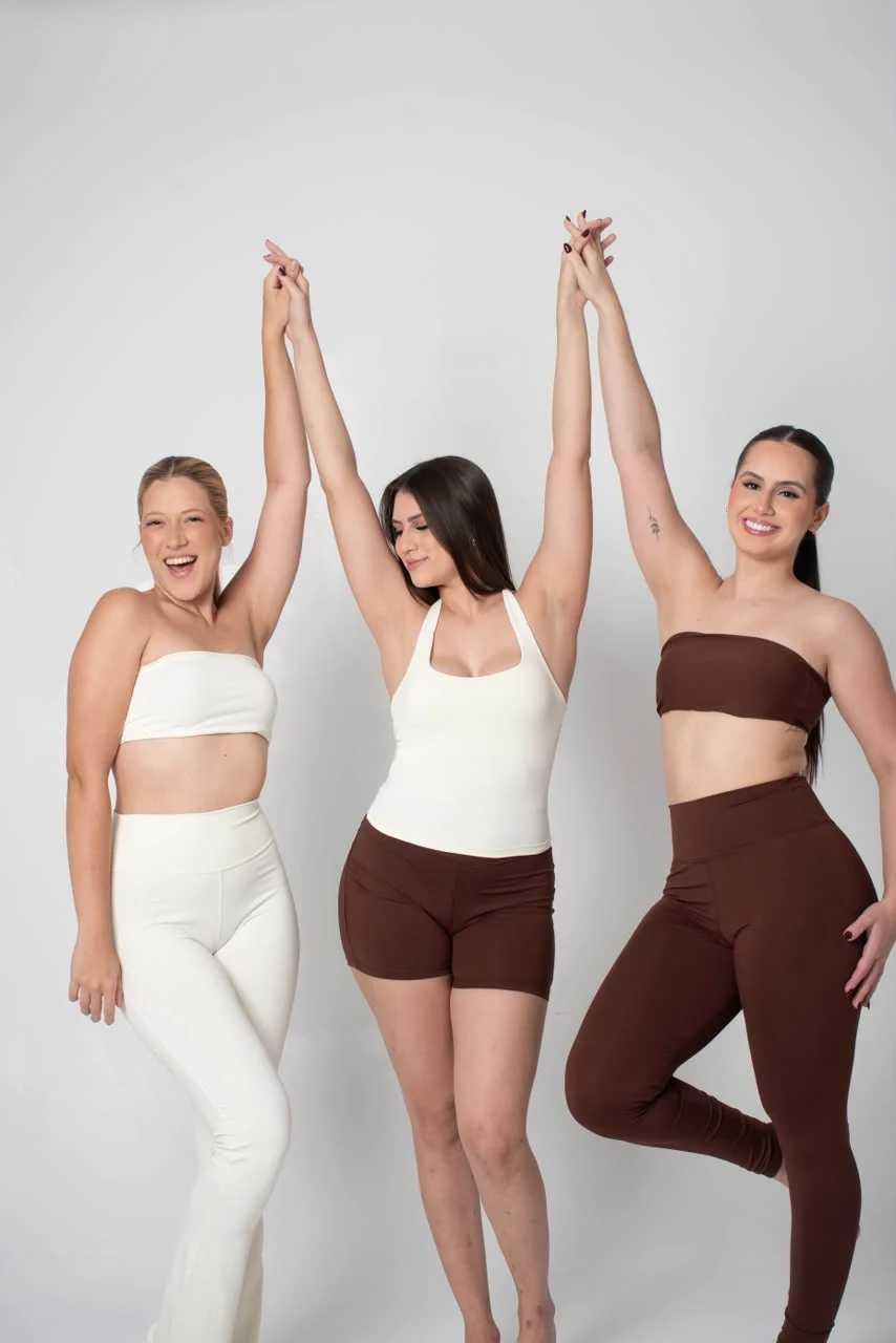 Três mulheres de mãos dadas erguidas, em conjuntos Along Active off-white e marrom